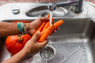 Hands rinsing carrots under a running kitchen sink faucet in a Baker, Denver home