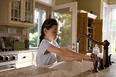 Child washing hands under running faucet in Castle Rock home kitchen