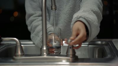 Woman filling up a glass of water at her kitchen sink in Cherry Hills Village