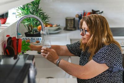 Woman filling up her drinking glass at kitchen sink