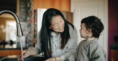 Mother with son in front of running kitchen faucet